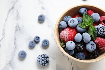 Bowl of frozen berries with mint leaves on white grunge background