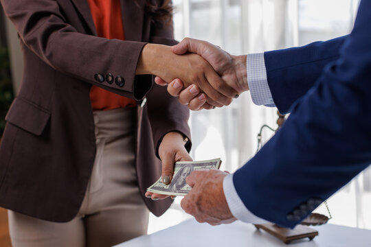 Concepts of corruption, handshake Corrupt lawyers shaking hands while exchanging bribe money after making agreement in the courtroom
