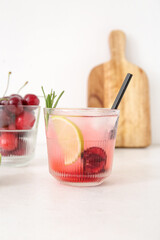 Glass of tasty cherry lemonade with lime and rosemary on white background
