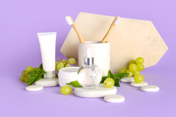 Composition with cosmetic products, toothbrushes and grapes on lilac background