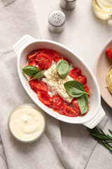 Baking dish with tasty tomatoes and feta cheese on light background