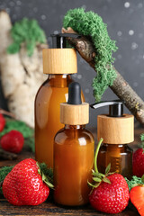 Composition with bottles of cosmetic products, strawberry and moss on wooden table, closeup