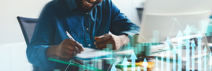 A man is focused on writing notes and creating business graphics at a modern desk. He smiles as he develops ideas to enhance his projects. Digital charts and growth graphics overlay the scene.