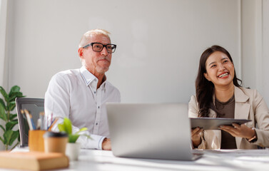 Team of happy business professionals engaged in a meeting, taking notes and collaborating in a sunlit office with lush indoor plants. Bright atmosphere and teamwork.
