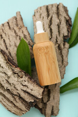 Bottle of essential oil, tree bark and plant leaves on color background, closeup