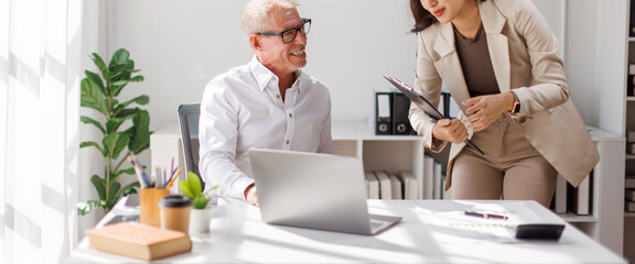 Team of happy business professionals engaged in a meeting, taking notes and collaborating in a sunlit office with lush indoor plants. Bright atmosphere and teamwork.
