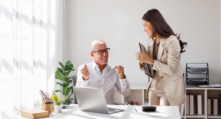 Team of happy business professionals engaged in a meeting, taking notes and collaborating in a sunlit office with lush indoor plants. Bright atmosphere and teamwork.
