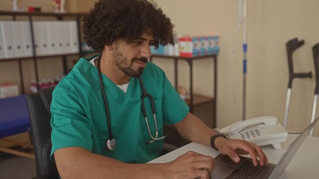 Man doctor in green scrubs with stethoscope typing on laptop and later folding arms at desk in building; calm concentration.