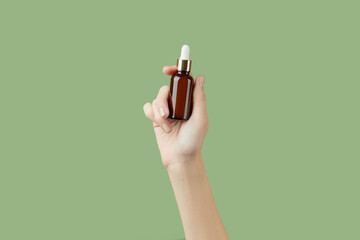 A womans hand holding a brown bottle of serum on a green background
