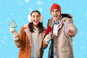 Cute young couple in warm clothes with passports and tickets on blue background. Winter vacation...