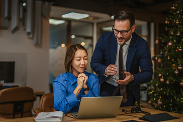 Diverse business colleagues collaborating on laptop in a festive office