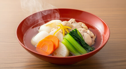 Steaming bowl of ozōni featuring soft mochi, chicken, daikon, carrots, and greens in a clear broth, garnished with fresh yuzu peel.