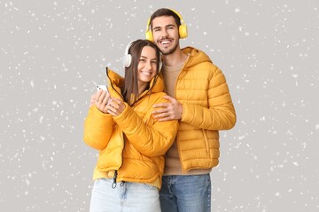 Loving couple in winter clothes, with headphones and mobile phone on grey background with snow