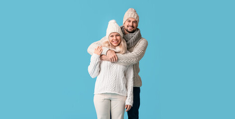 Happy couple in winter clothes hugging on blue background