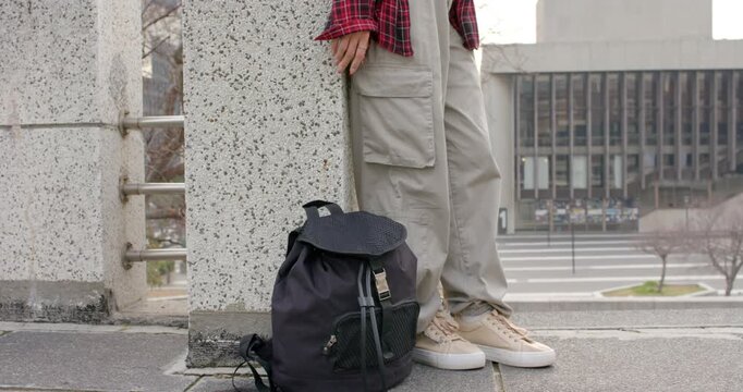 Upon lowering backpack person is lifting right foot and bracing sneaker against pillar balancing