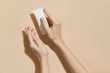 A womans hands holding a white cosmetic tube on a beige background. Beauty treatment concept