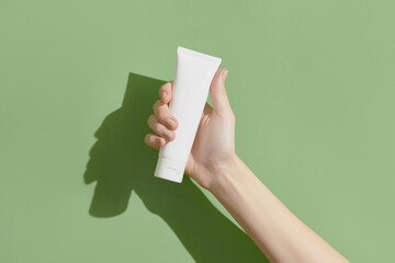 A womans hand holding a white cosmetic tube on a green background