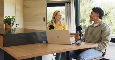 Female host greeting male co-host at wooden table, sparking playful banter around laptop microphone
