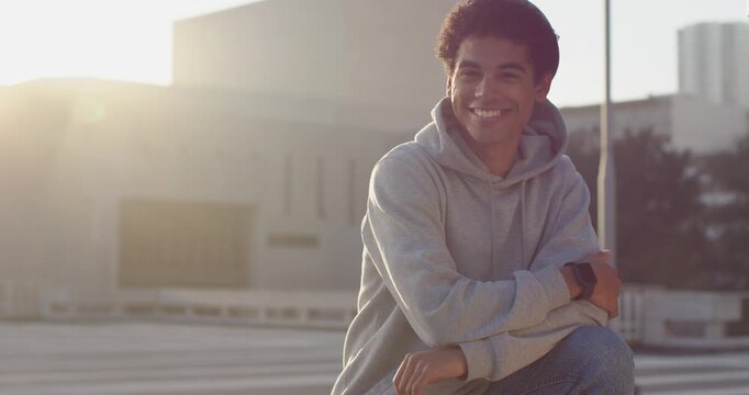 Seated man wearing hoodie, smiling, laughing while sun flare appearing on rooftop ledge, copy space
