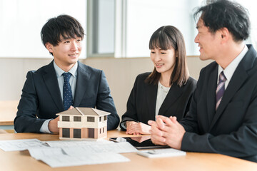 Male and female businessmen having a meeting while looking at a house model and blueprints