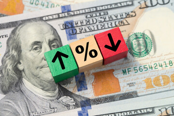 Wooden blocks with up, down, and percent symbols rest on U.S. currency, illustrating changing federal interest rate trends and financial market movement.