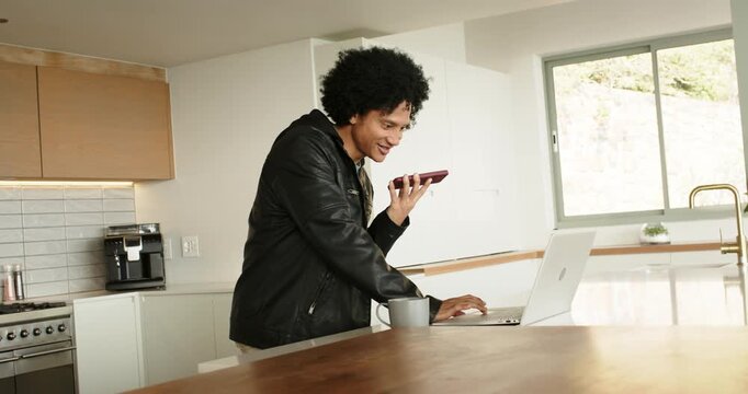 Man entering kitchen juggling smartphone call and laptop typing at kitchen island to update work