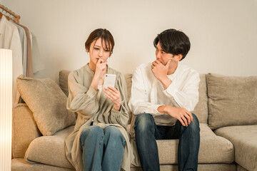 A couple who are shocked and surprised when looking at their smartphone on the sofa