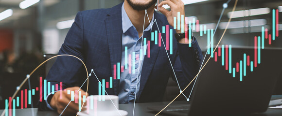 A successful middle eastern businessman in an expensive blue suit works on his laptop. He is smiling while having a phone conversation, engaged in a business discussion.