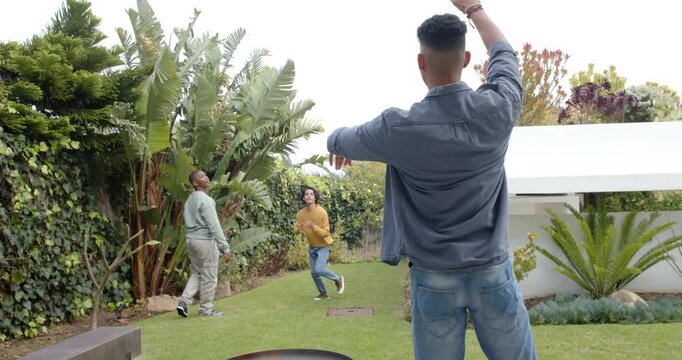 After windup by chambray shirted thrower diverse male friends tossing football in backyard catch
