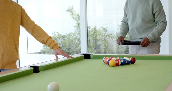 After game start, diverse male friends stepping up to rack balls at pool table before breaking