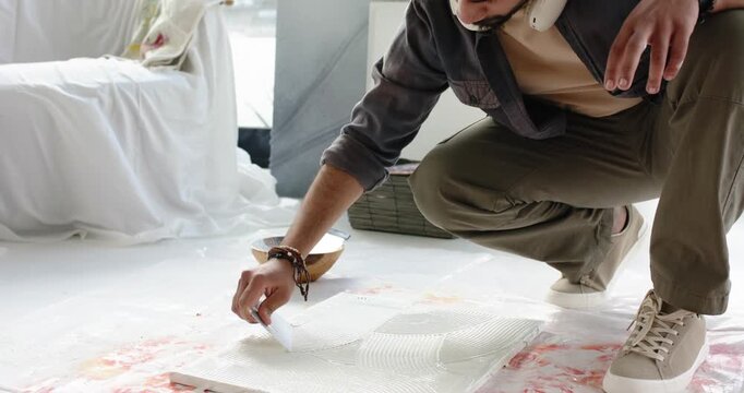 After scooping paste artist is spreading with notched trowel to create ridges on board in studio