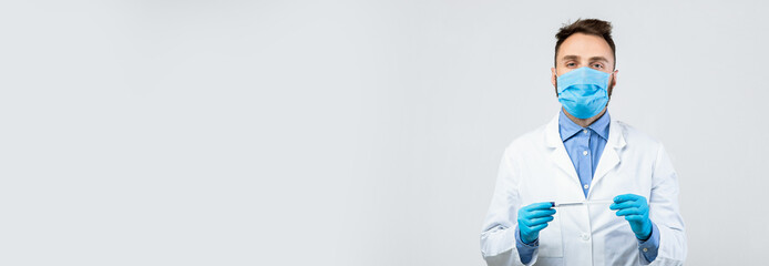 A laboratory technician in a white coat holds a syringe while wearing a blue mask and gloves. The scene captures a moment in a medical facility, emphasizing safety and professionalism.