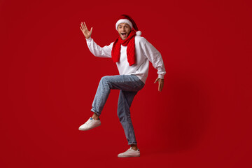 A joyful man dressed in a Santa hat and red scarf is dancing playfully against a bold red backdrop. His lively movement and smile capture the festive spirit of the holiday season.