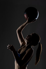 Athletic young woman in sports attire posing with a basketball, highlighting her silhouette and physique