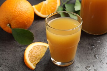 Fresh orange juice, fruits and leaves on grey table, closeup