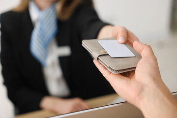 Receptionist giving passport and hotel key card to guest at reception desk indoors, closeup