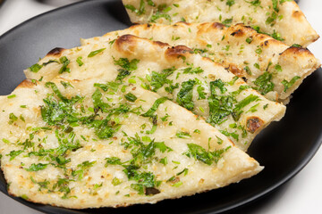 A plate of Indian garlic naan flat bread covered in fresh, chopped cilantro or coriander leaves and butter or ghee