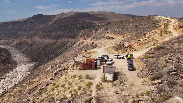 Aerial view of driving cars in dry valley in the island of Socotra. Motion drone video of moving cars on bumpy road surrounded by stones and dessert plants. Following cars from the air. Off-road drive