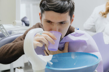A young male patient rinses his mouth in a dental office.