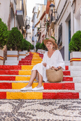 Young woman in a white dress sitting on the colourful Spanish Steps in the historic Arrabal district of Calpe, Spain
