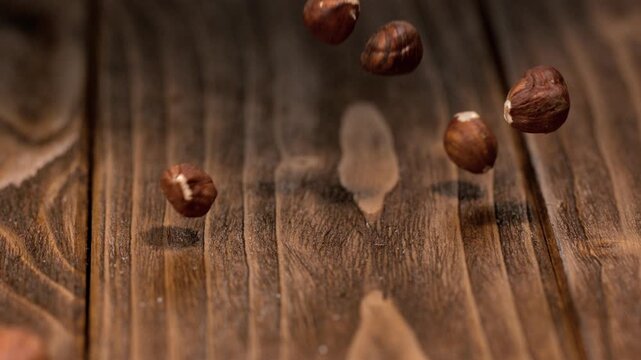 Hazelnuts drop onto wooden table in slow motion during a cooking demonstration
