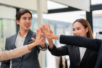 A team of successful Asian businesspeople shake hands and celebrate successful teamwork and goal achievement.