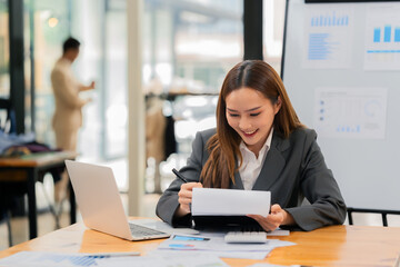 A businesswoman is working on a laptop and financial documents while her team is working behind her.