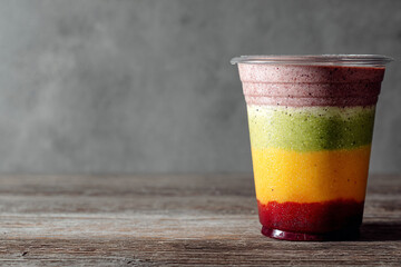Multi-layered fruit and vegetable smoothie with rich colors on a wooden surface against a gray wall.