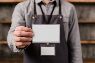 Person wearing an apron holds up a blank white ID card in a clear plastic holder, ready for corporate branding or name.