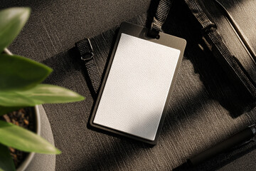Blank black corporate ID card holder with a white insert, lanyard attached, on a dark textured desk next to a plant.