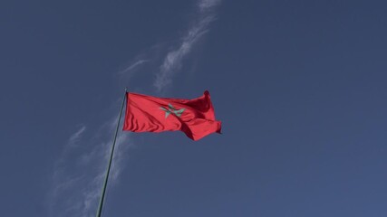 The Moroccan flag moving under a blue sky with a few clouds.