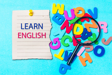 English letters scattered on blue background. Concept of cognitive development, grammar. Magnifying glass placed on English letters.