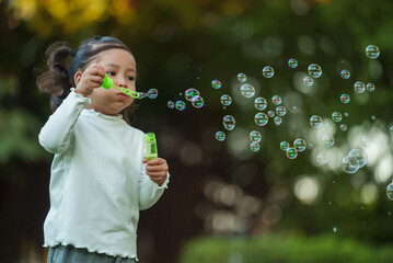 happy toddler girl blowing soap bubbles in park