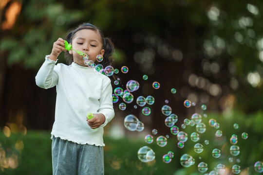 happy toddler girl blowing soap bubbles in park - Powered by Adobe
